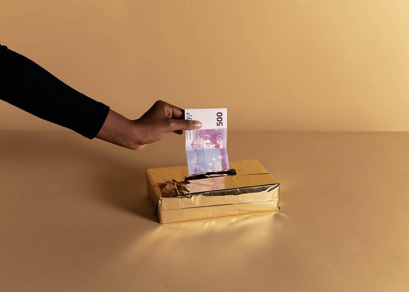 person putting money inside the gold box